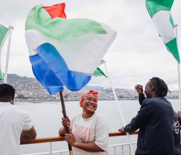 Fatoumata Sanoh, Galley Staff, waves the Sierra Leon flag as the Global Mercy enters the port in Freetown. Sanoh is from both Guinea and Sierra Leone.
